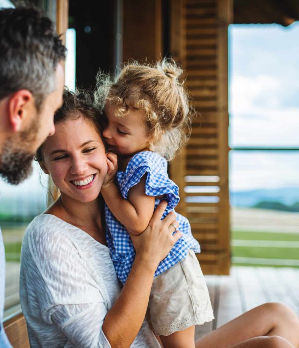 Family,With,Small,Daughter,Sitting,On,Patio,Of,Wooden,Cabin,